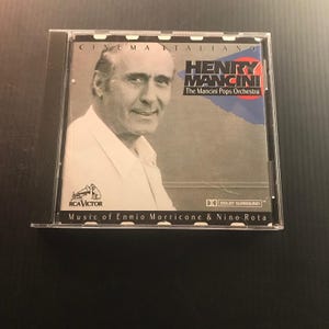 May include: A CD case featuring a portrait of Henry Mancini. The cover includes the text "CINEMA ITALIANO" and "HENRY MANCINI The Mancini Pops Orchestra." The CD is labeled "Music of Ennio Morricone & Nino Rota" and includes the RCA Victor logo.