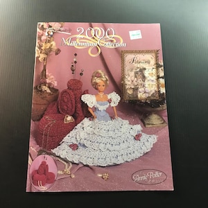 May include: A magazine cover featuring a doll in a white lace dress, part of the "2000 Millennium Collection." The cover has a pink background with floral and decorative elements. The doll has blonde hair and is wearing a blue and white dress.
