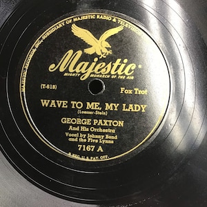 May include: A black vinyl record with a gold label. The label features a golden eagle with the text "Majestic, Mighty Monarch of the Air" and "Fox Trot". The record title is "Wave to Me, My Lady" by George Paxton and His Orchestra. The record number is "7167 A".