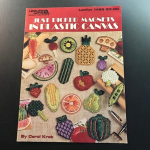 May include: A craft leaflet titled "Just Picked Magnets in Plastic Canvas" featuring various embroidered fruit and vegetable magnets. The cover includes a carrot, watermelon, strawberry, and other colorful designs.