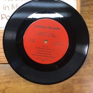 Peut inclure: Un disque vinyle noir avec une &eacute;tiquette rouge. L'&eacute;tiquette indique "Scholastic Records" et "Favorite Rhymes from A Rocket in My Pocket".