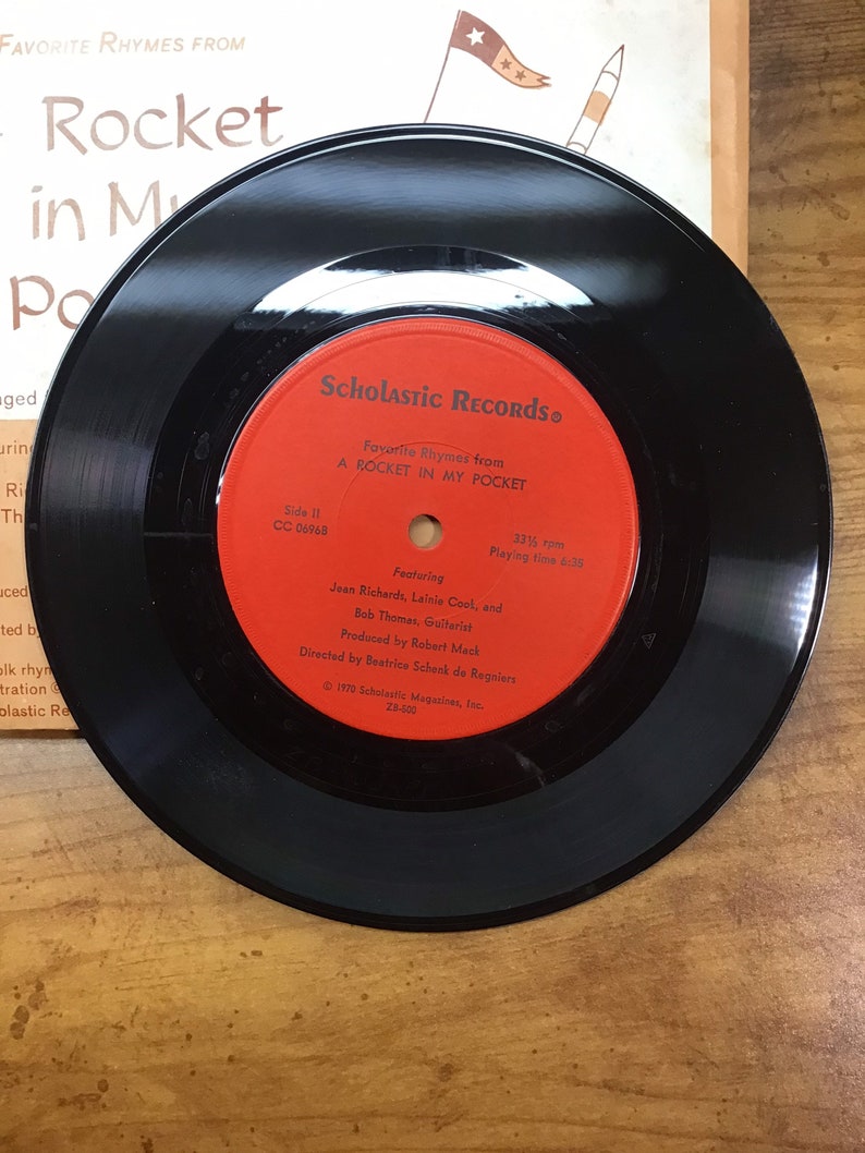 Peut inclure: Un disque vinyle noir avec une &eacute;tiquette rouge. L'&eacute;tiquette indique "Scholastic Records" et "Favorite Rhymes from A Rocket in My Pocket".