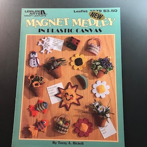 May include: A craft leaflet titled "Magnet Medley in Plastic Canvas" featuring various handmade plastic canvas magnets. The magnets include a snowman, flowers, fish, and a sun. The leaflet is from Leisure Arts.