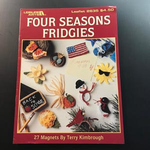 May include: A red book cover with the title "FOUR SEASONS FRIDGIES" and various crochet magnets. The magnets include a butterfly, American flag, snowman, and a cardinal. The text "BACK TO SCHOOL" is also visible.