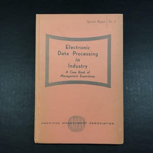 May include: A vintage book titled "Electronic Data Processing in Industry" with the subtitle "A Case Book of Management Experience." The cover is peach-colored with a gray frame around the title. The American Management Association logo is at the bottom.