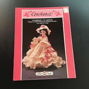 May include: A vintage crochet pattern book titled "Constance" featuring a doll in a cream-colored crochet dress with pink ribbons and a matching hat. The cover is pink with the text "Fashion Classics" and "Use with 15" Doll."