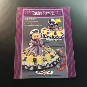 May include: A craft pattern book titled "Easter Parade" featuring crochet doll outfits. The cover shows a doll in a purple dress with a yellow skirt, a bonnet, and a basket of Easter eggs. The book includes instructions for a 13" music box doll and a 10 1/2" pillow doll.