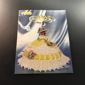 May include: A crochet pattern book titled "2003 Ribbons and Lace May Flowers" featuring a doll in a yellow and white crocheted dress and hat. The cover has a blue background and the Annie Potter Original logo.