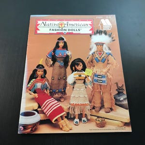 May include: A pattern booklet titled Native American Fashion Dolls by Annie's Attic featuring four dolls dressed in intricate, crocheted outfits with fringe, beadwork, and feathers. The cover displays colorful, detailed garments and accessories.