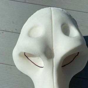 Pu&ograve; includere: Maschera di schiuma bianca con due fori per gli occhi e un foro per il naso. La maschera ha linee nere disegnate attorno ai fori per gli occhi.