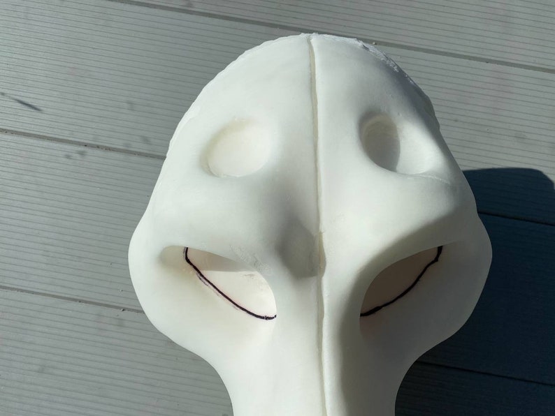 Pu&ograve; includere: Maschera di schiuma bianca con due fori per gli occhi e un foro per il naso. La maschera ha linee nere disegnate attorno ai fori per gli occhi.