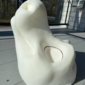 Pu&ograve; includere: Scultura bianca stampata in 3D con una forma organica liscia. La scultura ha una grande apertura nella parte superiore e una apertura pi&ugrave; piccola sul lato. La scultura &egrave; appoggiata su una superficie grigia.