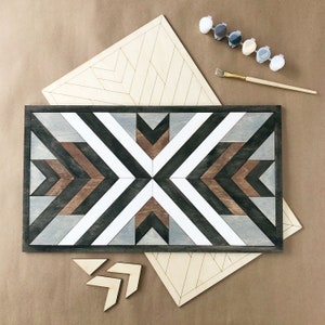 May include: A geometric wooden wall art piece with a black, white, brown, and grey colour scheme. The art is made up of multiple wooden pieces that are arranged in a geometric pattern. The art is unfinished and ready to be painted.
