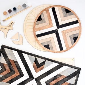May include: Two wooden wall decor pieces with a geometric pattern of black, white and brown stripes. The larger piece is round and the smaller piece is rectangular.