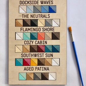 May include: A wooden board with a paint colour chart. The chart is labelled with the names "Dockside Waves", "The Neutrals", "Flamingo Shore", "Cozy Cabin", "Southwest Sun", and "Aged Patina". Each label has a row of small painted wood samples.