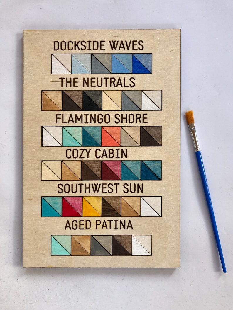 May include: A wooden board with a paint colour chart. The chart is labelled with the names "Dockside Waves", "The Neutrals", "Flamingo Shore", "Cozy Cabin", "Southwest Sun", and "Aged Patina". Each label has a row of small painted wood samples.