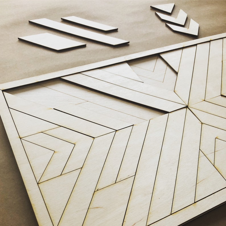 May include: A geometric wood wall art piece with a light wood finish and a black outline. The design features a series of intersecting lines creating a complex pattern.