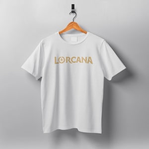 May include: White t-shirt with a gold graphic of a stylized star and the word "LORCANA" printed on the front.