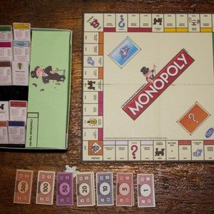 May include: A Monopoly board game set, featuring a game board, property cards, money, and a box with property deeds. The board game is on a wooden surface. The word "MONOPOLY" is prominently displayed on the board.