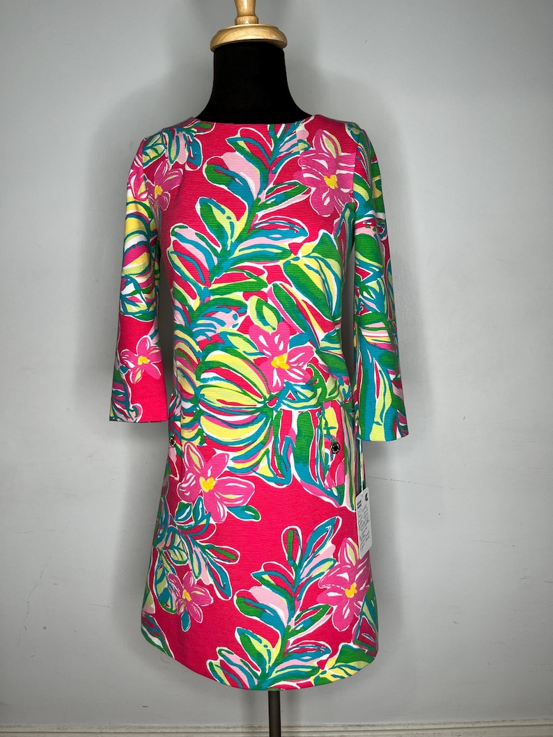 May include: A pink dress with a tropical print featuring green leaves, pink and yellow flowers. The dress has a boat neck and 3/4 sleeves.