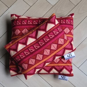 May include: Two red, orange, and white patterned fabric pillows with a triangular design. The pillows have a label that says "Beebe's Corn Bags".