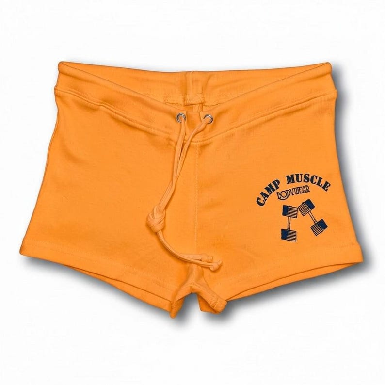 Puede incluir: Pantalones cortos de color naranja brillante con cintura de cord&oacute;n y un gr&aacute;fico azul oscuro en la parte inferior derecha. El gr&aacute;fico muestra el texto CAMP MUSCLE BODYWEAR sobre una ilustraci&oacute;n de dos mancuernas inclinadas en forma de V.