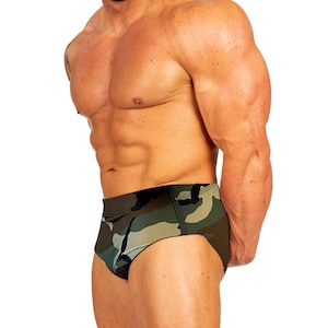 May include: Swim briefs with a camouflage pattern in green, brown, and black. The briefs have a low-rise cut and a streamlined design. The fabric appears to be a smooth, possibly synthetic material. The background is plain white.