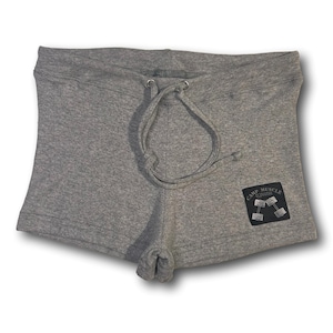 Puede incluir: Pantalones cortos de color gris jaspeado con cintura de cord&oacute;n y ojales met&aacute;licos plateados. Un parche rectangular negro est&aacute; cosido en la parte inferior derecha, mostrando el texto "CAMP MUSCLE" sobre una ilustraci&oacute;n gr&aacute;fica de dos mancuernas.