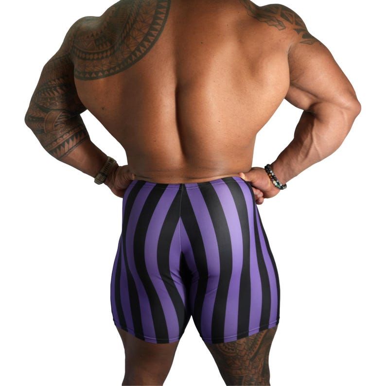 May include: Purple and black striped athletic shorts. The shorts have vertical stripes and a form-fitting design. The image shows the back of a person wearing the shorts, with a white background.