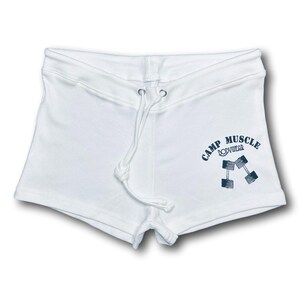 Puede incluir: Pantalones cortos deportivos blancos con cintura de cord&oacute;n y un gr&aacute;fico azul oscuro en la pierna derecha. El gr&aacute;fico muestra el texto CAMP MUSCLE BODYWEAR dispuesto en arco sobre una ilustraci&oacute;n de dos mancuernas cruzadas.