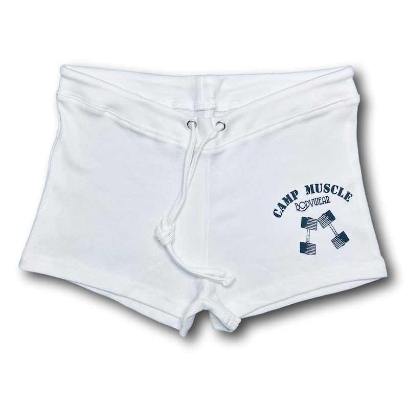Puede incluir: Pantalones cortos deportivos blancos con cintura de cord&oacute;n y un gr&aacute;fico azul oscuro en la pierna derecha. El gr&aacute;fico muestra el texto CAMP MUSCLE BODYWEAR dispuesto en arco sobre una ilustraci&oacute;n de dos mancuernas cruzadas.
