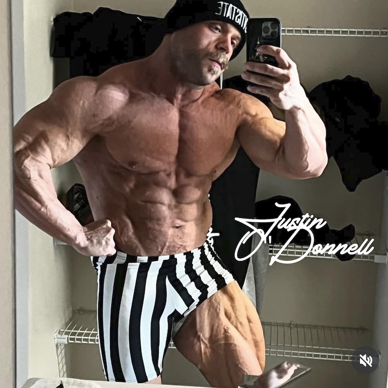 May include: A muscular person wearing black and white striped shorts and a black beanie with white text. The person is flexing in front of a mirror, holding a phone. The name "Justin Donnell" is written in cursive.