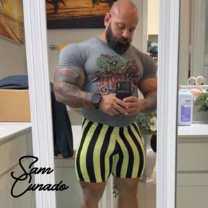 May include: A person wearing a gray t-shirt with a colorful graphic and black and yellow striped shorts. The person is holding a phone and looking into a mirror. The text "Sam Cunado" is in the lower left corner.