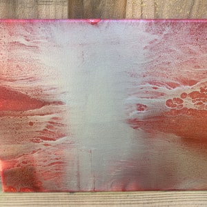 Op de afbeelding: Abstract schilderij op canvas met een rood en zilver kleurenschema. De verf is aangebracht in een vloeiende, gelaagde stijl, waardoor een uniek en getextureerd oppervlak ontstaat.