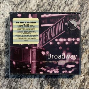 May include: A Broadway CD featuring the Great Original Cast Recordings. The cover displays a street sign with the word "Broadway" in white, set against a blurred background. The CD case includes a sticker with details about the recordings.