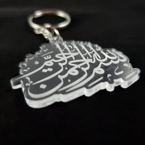 May include: A clear acrylic keychain with a white Arabic inscription. The inscription is in the shape of a heart.