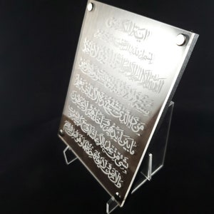 May include: A silver acrylic plaque with an engraved Islamic prayer in Arabic script. The plaque is displayed on a clear acrylic stand.