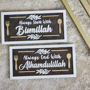 May include: Two framed wooden signs with a brown background and white lettering. The top sign says "Always Start With Bismillah" and the bottom sign says "Always End With Alhamdulillah". Both signs have a gold fork and spoon on them.