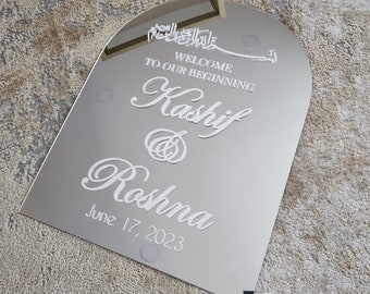 May include: A silver arched mirror with the text "Welcome to our beginning Kshif & Roshna June 17, 2023" in white lettering.