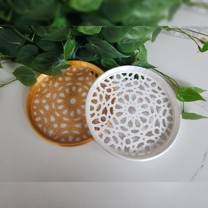 May include: Two decorative round trays with intricate geometric designs. The larger tray is white with a white design, and the smaller tray is gold with a gold design.