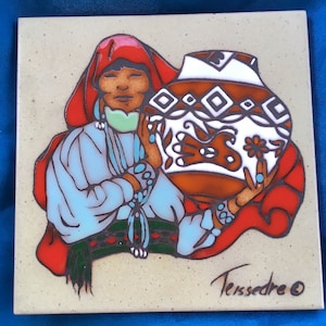 May include: Square ceramic tile featuring a Native American woman holding a decorated pot. The woman wears a red head covering, turquoise jewelry, and a light blue top. The pot is brown with white and black geometric designs. The tile is signed "Terssedre".