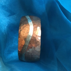 May include: A hammered copper bracelet with a silver band. The bracelet is a wavy design and has a rustic look.