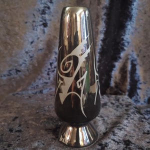 May include: A vintage black and silver vase with a flared base and a tall, slender body. The vase features a silver, stylized design on the front. The vase is approximately 8 inches tall.