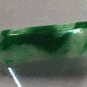 Può includere: Un cabochon di giada verde e bianco lucido e liscio con un motivo a spirale. Il cabochon è di forma ovale e ha una finitura lucida.