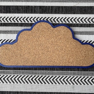 May include: A blue and brown corkboard shaped like a cloud. The corkboard is on a black and white striped background.