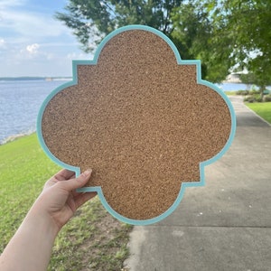 May include: A light blue cork board with a decorative, scalloped edge. The board is made of cork and has a natural brown colour.