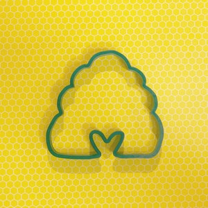 May include: Green plastic cookie cutter shaped like a beehive with a small heart-shaped opening at the bottom.