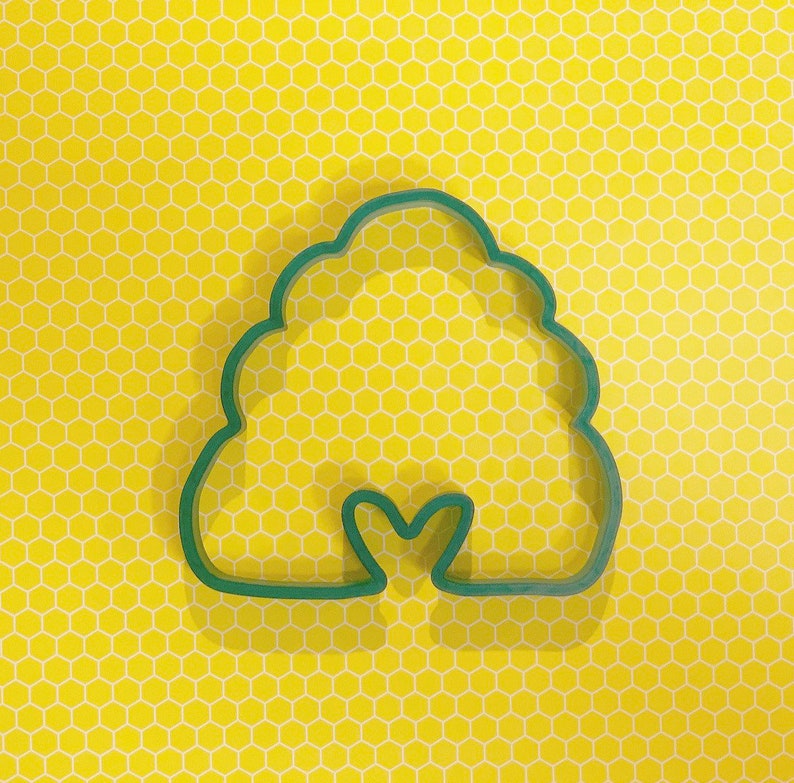 May include: Green plastic cookie cutter shaped like a beehive with a small heart-shaped opening at the bottom.