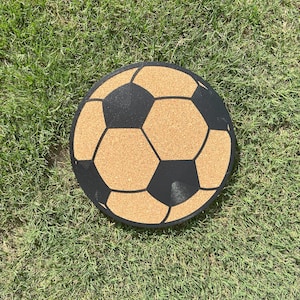 May include: A cork board in the shape of a football with black lines and a brown cork surface.
