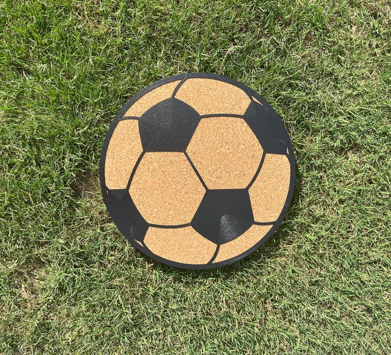 May include: A cork board in the shape of a football with black lines and a brown cork surface.